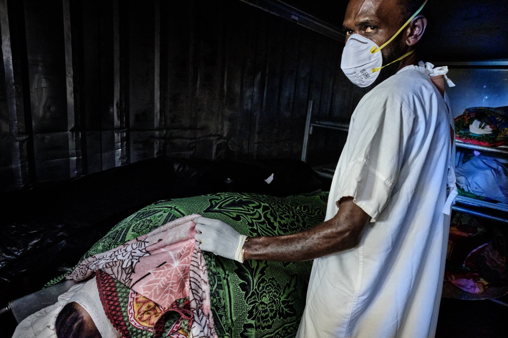 WP36307 A man wearing a face mask cover a body in a morgue